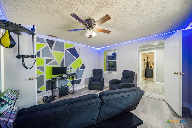 living room featuring baseboards, a textured ceiling, ceiling fan, and wood finished floors