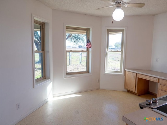 unfurnished office with a textured ceiling, ceiling fan, and built in desk