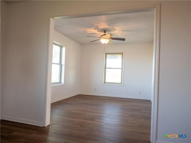 empty room featuring ceiling fan, a textured ceiling, dark hardwood / wood-style flooring, and a healthy amount of sunlight