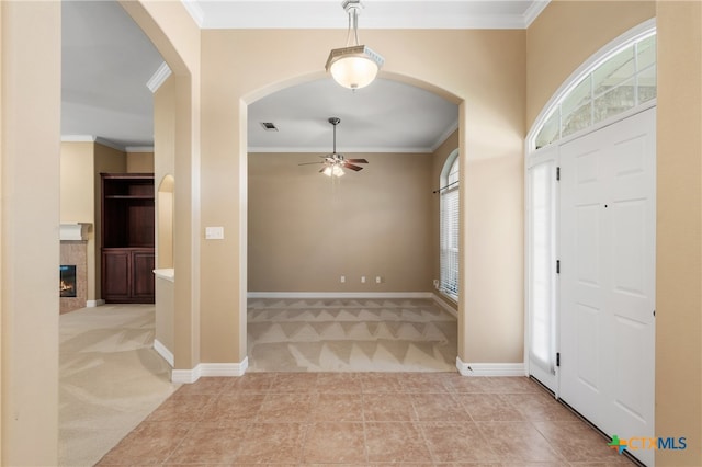 carpeted foyer featuring a fireplace, a wealth of natural light, ceiling fan, and crown molding