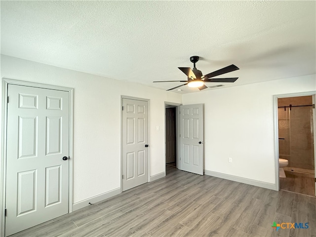 unfurnished bedroom with ceiling fan, ensuite bathroom, a textured ceiling, and light wood-type flooring