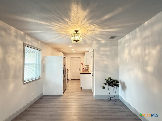 hallway with sink, a notable chandelier, and light hardwood / wood-style floors