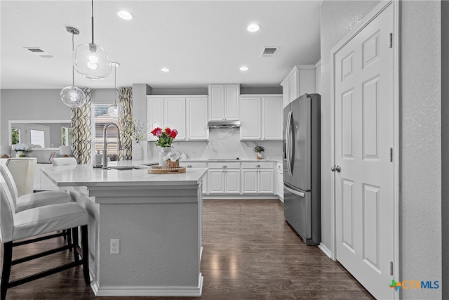 kitchen featuring stainless steel fridge, white cabinetry, sink, an island with sink, and dark wood-type flooring