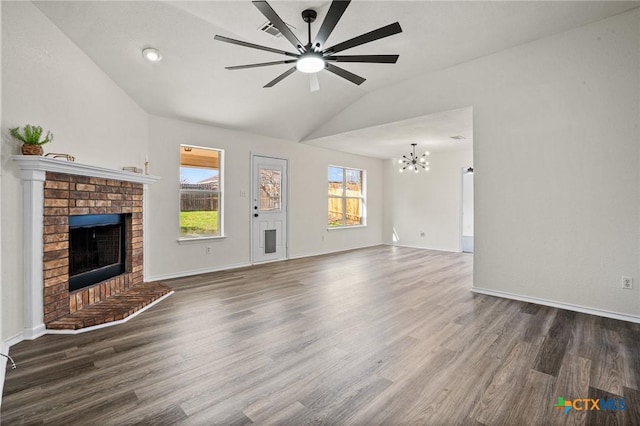 unfurnished living room with ceiling fan with notable chandelier, a brick fireplace, lofted ceiling, and dark hardwood / wood-style floors