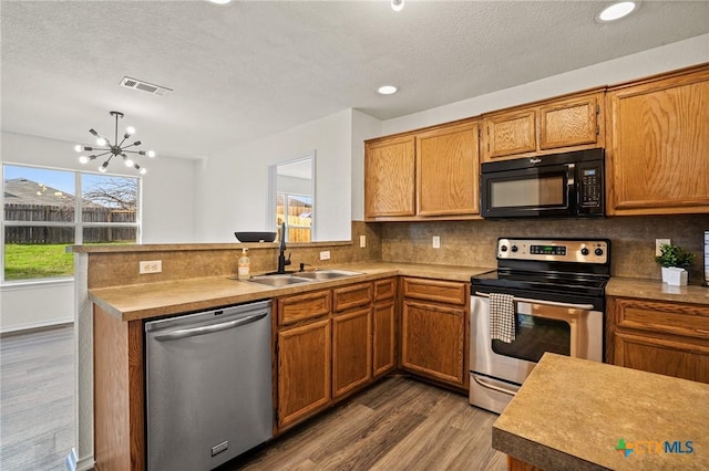 kitchen with sink, hardwood / wood-style floors, kitchen peninsula, a chandelier, and appliances with stainless steel finishes