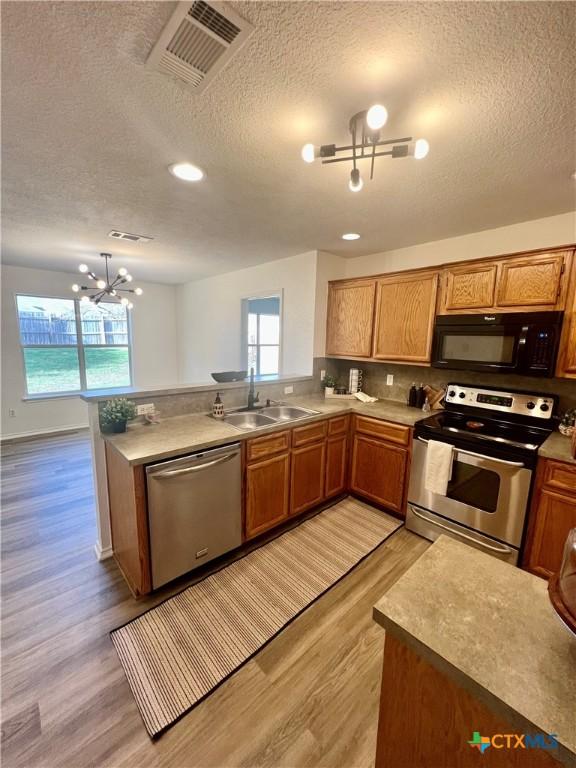 kitchen with kitchen peninsula, stainless steel appliances, a notable chandelier, light wood-type flooring, and sink