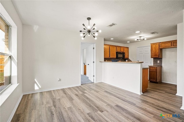 kitchen with a chandelier, hanging light fixtures, light wood-type flooring, kitchen peninsula, and tasteful backsplash