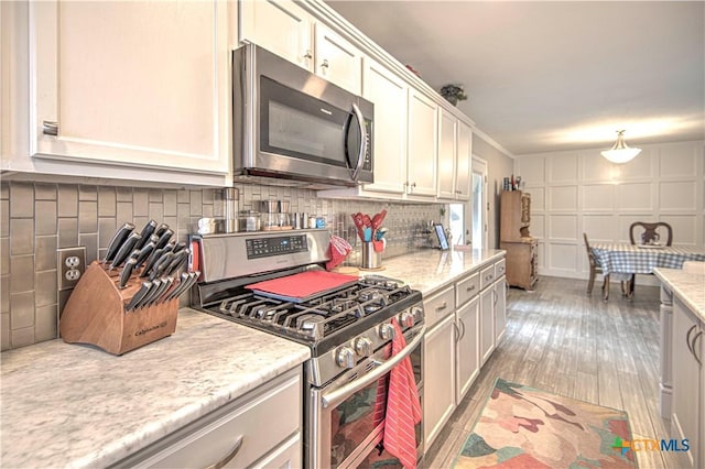 kitchen with appliances with stainless steel finishes, light stone countertops, light hardwood / wood-style flooring, and backsplash