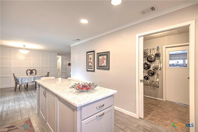 kitchen featuring crown molding, light stone countertops, a center island, and white cabinets