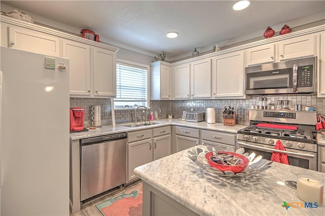 kitchen with tasteful backsplash, appliances with stainless steel finishes, sink, and light stone counters