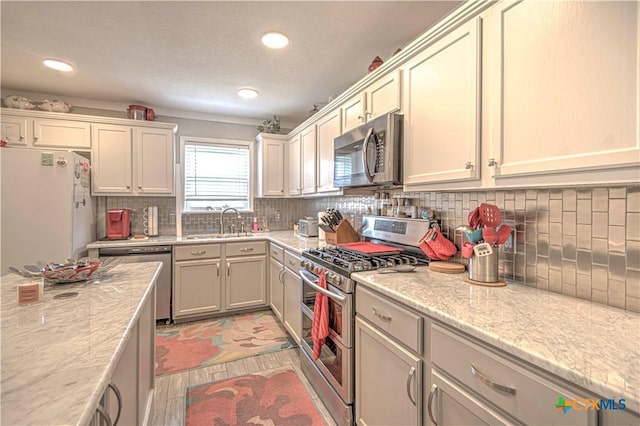 kitchen featuring sink, decorative backsplash, light stone counters, light hardwood / wood-style floors, and stainless steel appliances