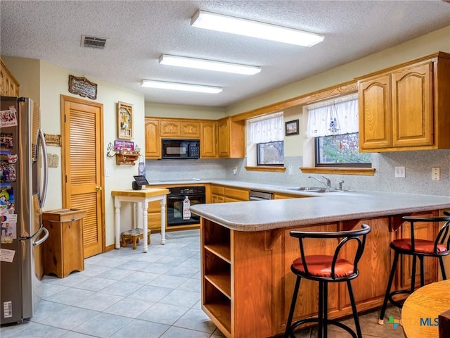 2904 Candace Cir, Horseshoe Bay, TX 78657 - kitchen with black appliances, a peninsula, a textured ceiling, light tile patterned floors, and a breakfast bar area