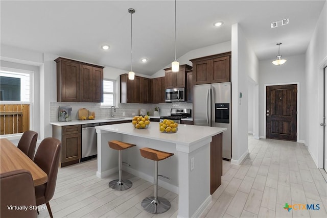 kitchen featuring pendant lighting, sink, lofted ceiling, appliances with stainless steel finishes, and a kitchen island