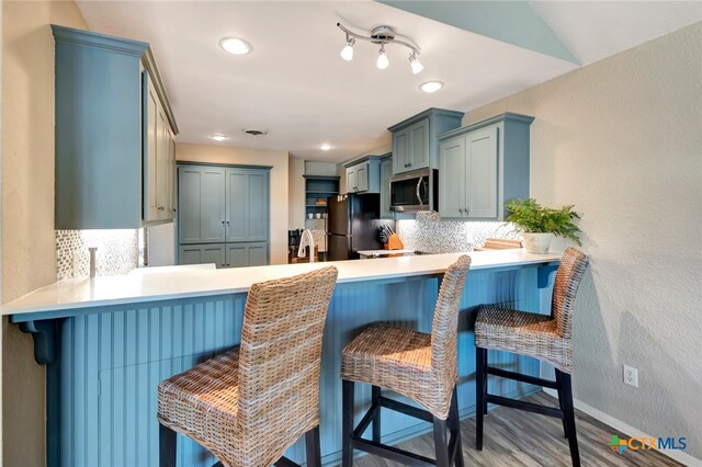 kitchen with kitchen peninsula, tasteful backsplash, black fridge, a breakfast bar, and hardwood / wood-style flooring