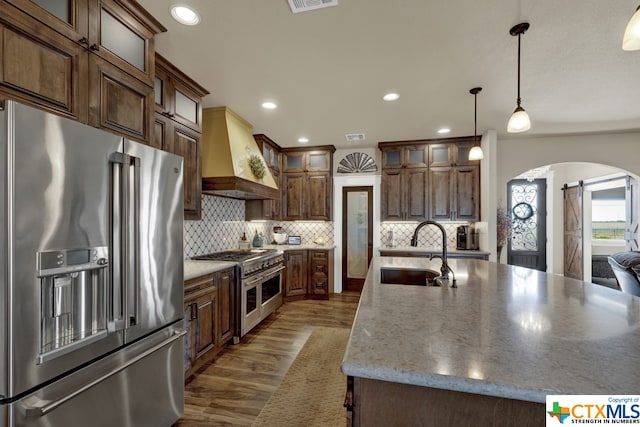 kitchen featuring a barn door, sink, custom exhaust hood, high end appliances, and a kitchen island with sink