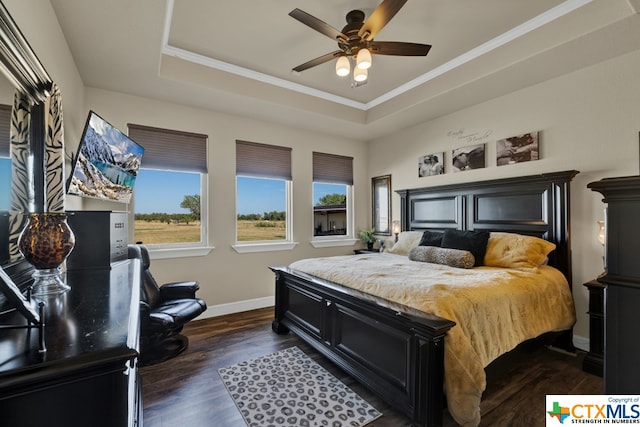 bedroom featuring dark wood-type flooring, ornamental molding, a tray ceiling, and ceiling fan