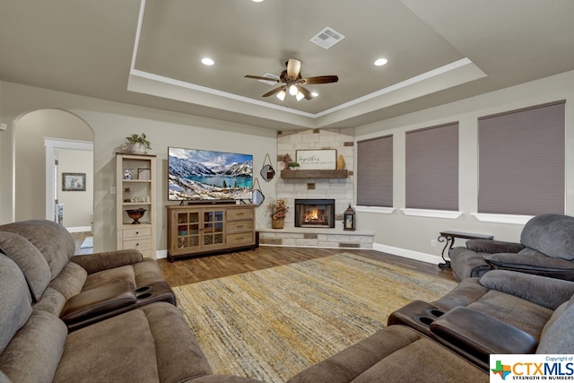 living room featuring a fireplace, wood-type flooring, ceiling fan, and a tray ceiling