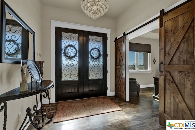 foyer entrance featuring dark wood-type flooring, a barn door, french doors, and a notable chandelier