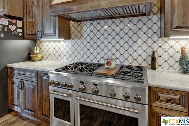 kitchen with double oven range, premium range hood, light hardwood / wood-style floors, and tasteful backsplash