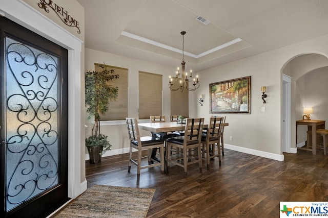 dining room with dark wood-type flooring, a raised ceiling, and an inviting chandelier