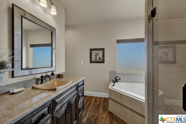 bathroom with vanity, a relaxing tiled tub, and wood-type flooring