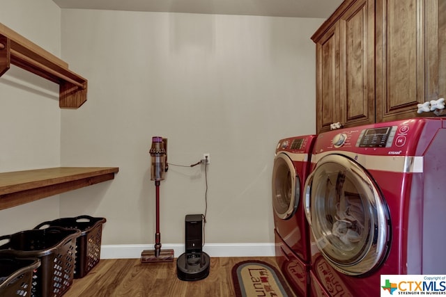 laundry room with washing machine and dryer, cabinets, and wood-type flooring