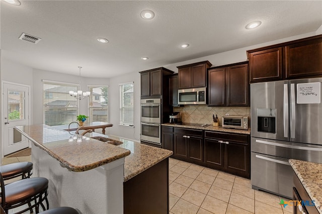 kitchen with appliances with stainless steel finishes, a chandelier, a kitchen island, pendant lighting, and decorative backsplash