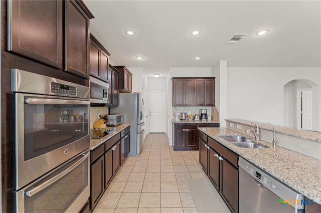 kitchen featuring sink, light tile patterned flooring, light stone countertops, dark brown cabinets, and appliances with stainless steel finishes