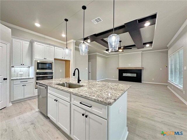 kitchen featuring a kitchen island with sink, built in microwave, sink, decorative light fixtures, and white cabinets