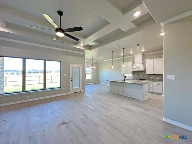 kitchen featuring pendant lighting, a center island with sink, white cabinets, ceiling fan with notable chandelier, and custom exhaust hood