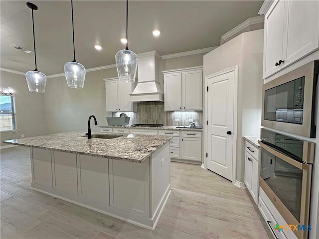 kitchen featuring pendant lighting, appliances with stainless steel finishes, a kitchen island with sink, and white cabinets