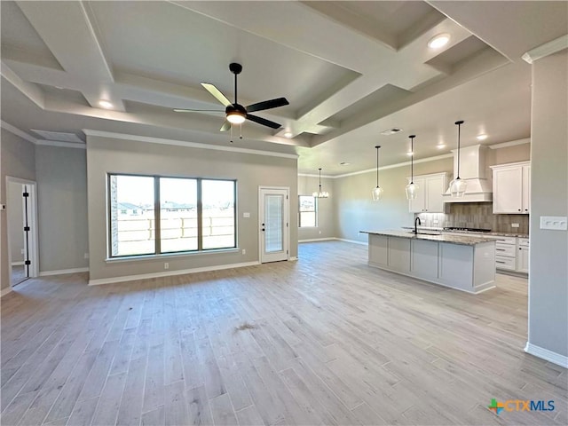 kitchen featuring custom exhaust hood, white cabinets, ceiling fan with notable chandelier, light wood-type flooring, and an island with sink