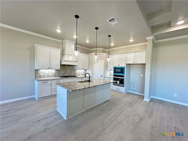 kitchen with decorative backsplash, light stone countertops, white cabinets, and an island with sink