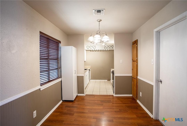 hall featuring visible vents, wainscoting, an inviting chandelier, and wood finished floors