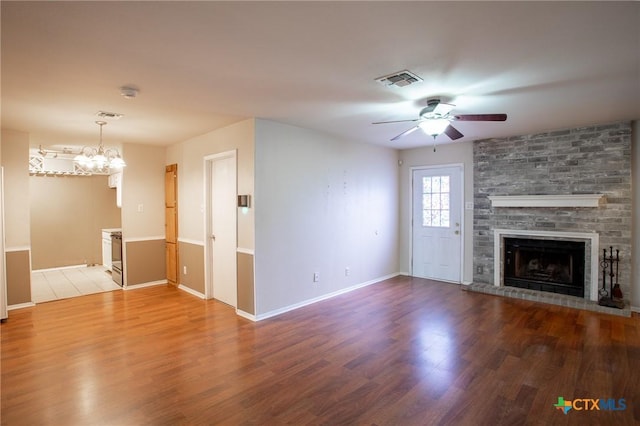 unfurnished living room with ceiling fan with notable chandelier, visible vents, light wood finished floors, and a large fireplace