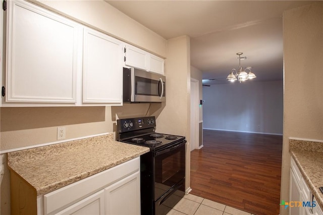 kitchen with stainless steel microwave, black range with electric stovetop, a chandelier, pendant lighting, and white cabinets