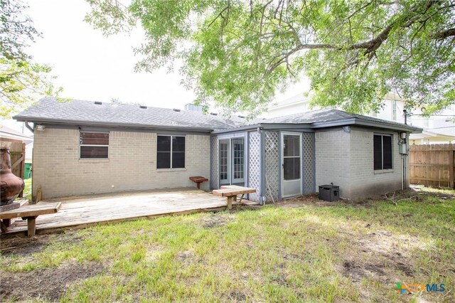 back of house with brick siding, a lawn, roof with shingles, and fence