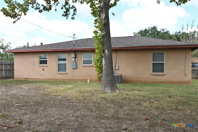 rear view of property featuring stucco siding, cooling unit, fence, a shingled roof, and a lawn