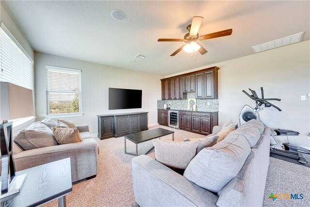 living room with beverage cooler, sink, light colored carpet, and ceiling fan