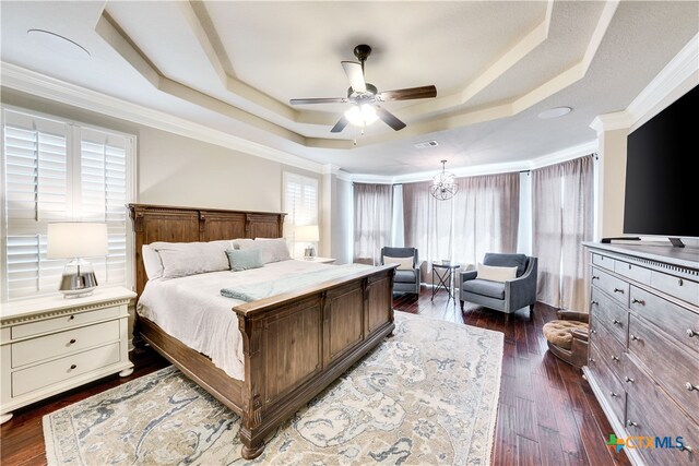 bedroom featuring dark wood-type flooring, ceiling fan with notable chandelier, crown molding, and a raised ceiling