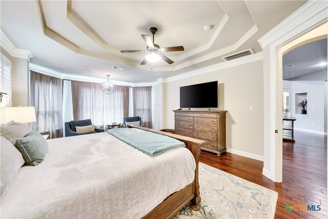 bedroom with dark wood-type flooring, a tray ceiling, ornamental molding, and ceiling fan with notable chandelier