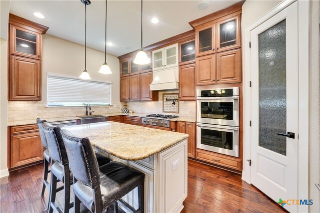 kitchen featuring light stone counters, stainless steel appliances, a kitchen island, custom range hood, and dark hardwood / wood-style flooring