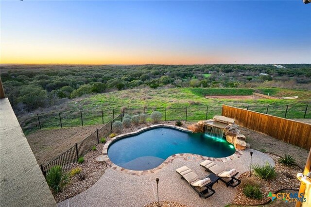 pool at dusk featuring a patio and pool water feature