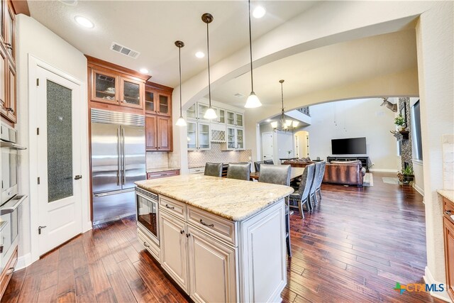 kitchen featuring dark wood-type flooring, built in appliances, pendant lighting, and light stone counters