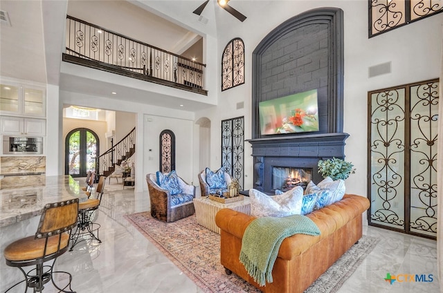 living room featuring a fireplace, ceiling fan, and a towering ceiling