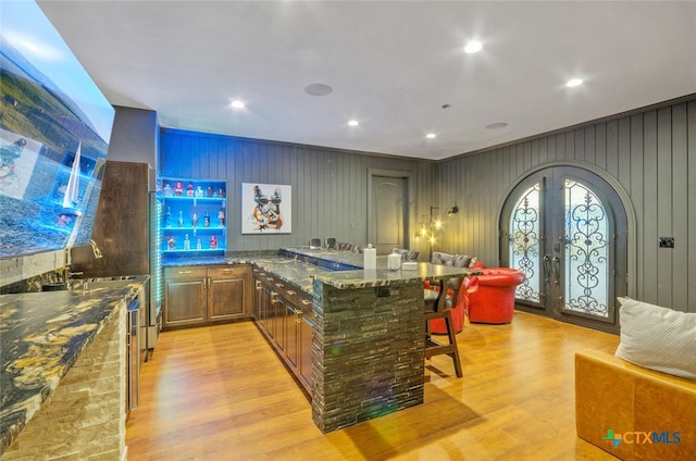 bar with light wood-type flooring, wooden walls, and dark stone countertops