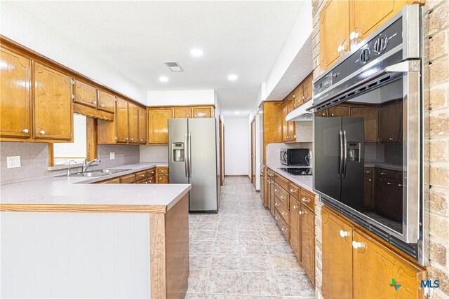 679 Royal Rd, Port Lavaca, TX 77979 - kitchen featuring stainless steel fridge, brown cabinetry, a sink, under cabinet range hood, and a peninsula