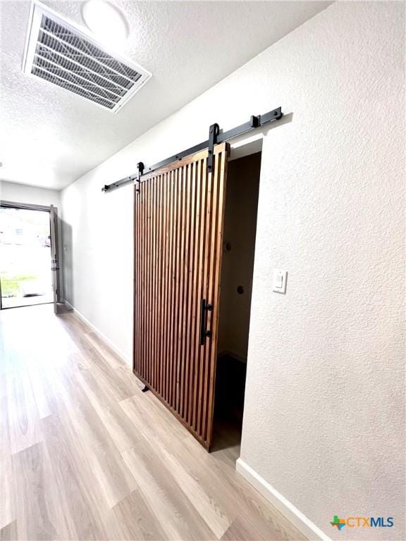 107 S 23rd St, Temple, TX 76504 - hall featuring a barn door, wood finished floors, a textured ceiling, baseboards, and a textured wall