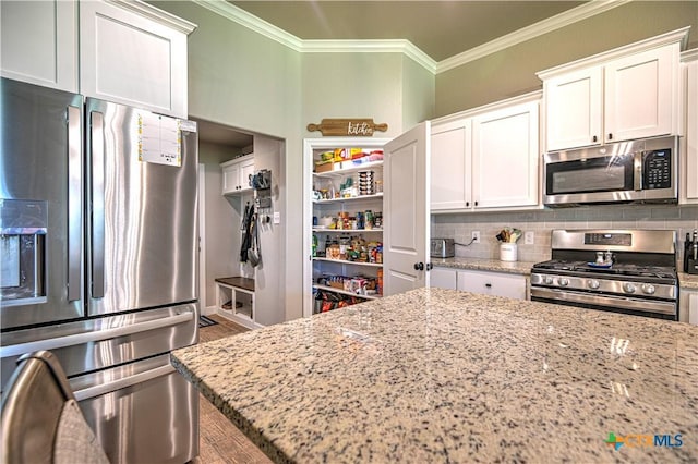 6129 Messina Dr, Temple, TX 76502 - kitchen with stainless steel appliances, ornamental molding, light stone counters, white cabinetry, and backsplash