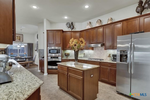 kitchen with a center island, under cabinet range hood, light stone counters, stainless steel appliances, and backsplash
